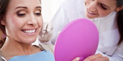 Woman looking at smile in mirror during dental cleaning visit