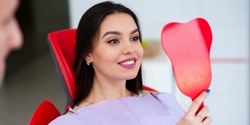 Woman looking at smile in mirror after makeover